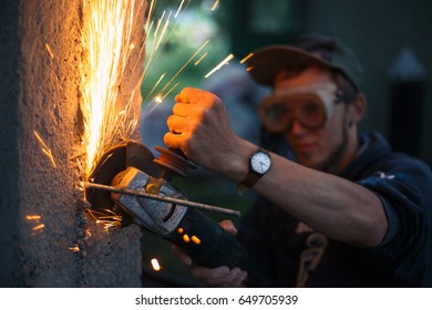 Man with a grinder is building a fence from wood and concrete at outdoor. Bright sparks are flying from cutting metal abrasive disk of the angle grinder. - Powered by Shutterstock