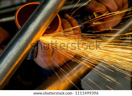 Man grinding steel tubing with pneumatic grinding disc showering sparks and hot slag