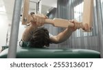 Man gripping pilates bar on reformer for upper body strength and control training during a workout at gym. Trainer doing swan dive on the cadillac for improving posture and core stability. Habituate.