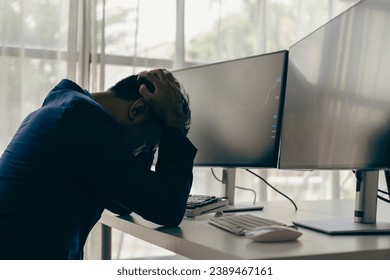 Man groans with hands on computer head with graph of unsuccessful business on monitor screen with cryptocurrency graph that tracks cryptocurrency prices.
