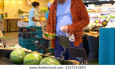A man in a grocery store in the fruit section chooses ripe, juicy and fresh pieces of watermelon. Man went shopping at the supermarket on the weekend. Selection of delicious watermelons at the market.