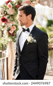 Man, groom and wedding day at reception for marriage commitment with flower arch, ceremony or event. Male person, husband and boutonniere on suit at love celebration for milestone, backyard or bowtie