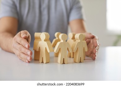 Man Guarding Small Wooden Human Figures. Close Up Of Male Hands And Little Pawn People On Desk. Responsible Team Leader Creates Safe Workplace And Protects His Employees. Corporate Safety Concept