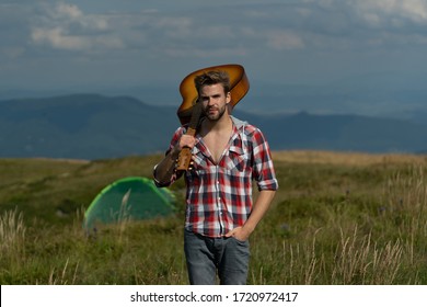 Man with guitar on camp. Campfire songs. Acoustic guitar player on countryside, music song. Sexy man with guitar in checkered shirt. Hipster fashion