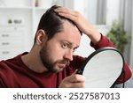 Man with hair loss problem looking at mirror indoors