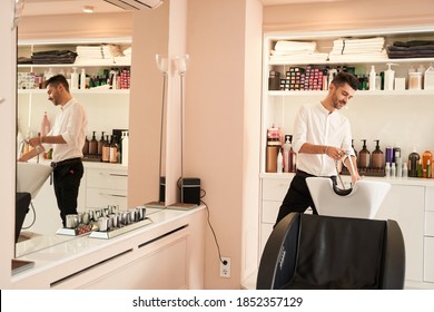 Man hairdresser preparing the workplace for working with a client at the salon. Young hairstylist wearing shirt while cleaning chair and washbasin in beauty studio - Powered by Shutterstock