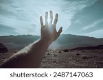 Man hand and arm reaching out blocking sun flare, muted colors, film edit, desert background, bright afternoon sunlight, dramatic or hopeful moment, Death Valley