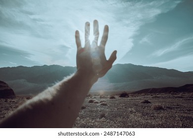 Man hand and arm reaching out blocking sun flare, muted colors, film edit, desert background, bright afternoon sunlight, dramatic or hopeful moment, Death Valley - Powered by Shutterstock