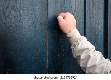 man hand in a beige jacket knocks on a blue wooden door Anybody home - Shutterstock ID 2123753924