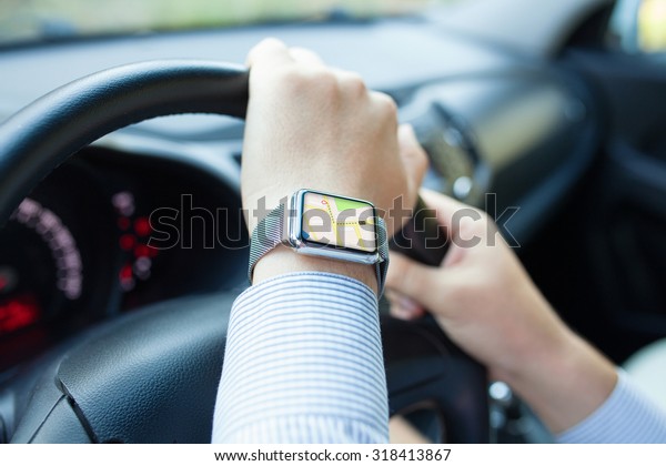 Man hand in the car with watch and app navigation\
on the screen