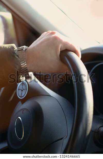 Man hand with clock driving  car holding black
steering wheel. Vertical
foto