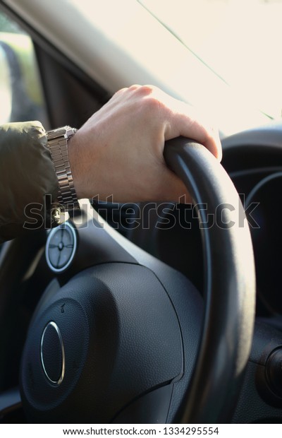 Man hand with clock driving  car holding black\
steering wheel. Vertical\
foto
