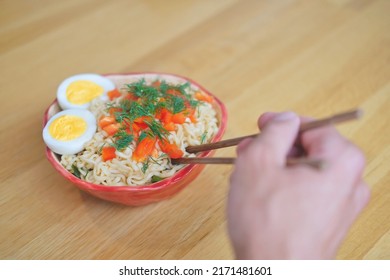 Man (hand) Eating Asian Egg Noodles In Red Bowl With Bamboo Chopsticks Close Up