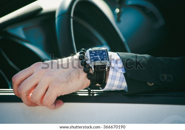 man hand in\
elegant suit with watch and bracelet lean on car window, closeup\
natural light, shallow depth of\
field