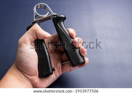 A man hand exercised with hand grip on a dark color background.