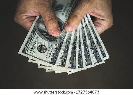 man hand giving 100 dollar bills isolated on dark background. Hand holding us dollar bills. Hands with money isolated on a dark background. American dollar bills being held out. Toned picture