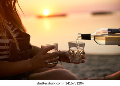 Man hand gracefully pouring white wine while girlfriend holding glasses. Couple enjoy beverage on sunset near sea. Romantic picnic with alcoholic drink on the beach. Friends relax on the shore. - Powered by Shutterstock