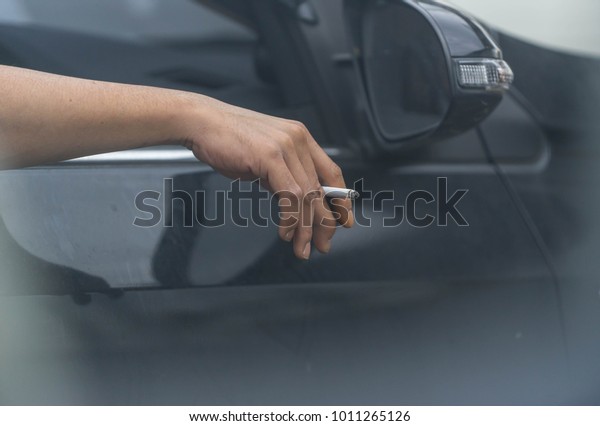 man ‘s hand hold burning cigarette outside car for\
smoke not come inside