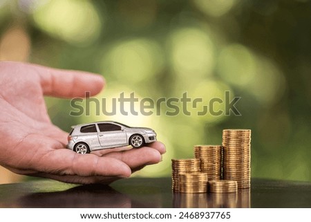 Man hand hold the car to the stack gold coin with growing the collect interest on the wood in the public park, Loan and saving for buy a car and business investment a chattel in the future concept.