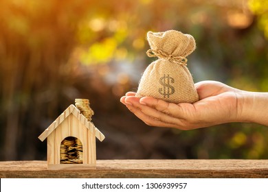 Man hand hold money bag with presenting and home model and gold coin with growing interest in the public park, Saving money for buy house or loan for plan business investment of real estate concept.