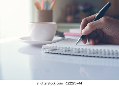 Man Hand Holding Black Pen Writing On Paper Notebook On Office Table, Close Up