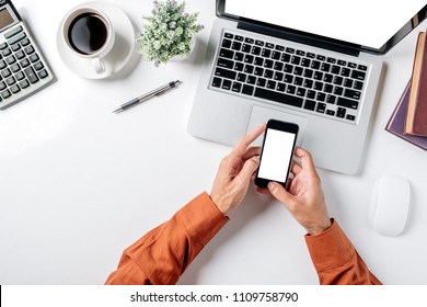 Man Hand Holding Blank Screen Smart Phone On White Desk Table With Laptop Computer,calculator,pen,notenook,cup Of Coffee And A Lot Of Things.Top View,Flat Lay.