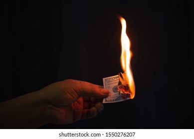 man hand holding burning dollar banknotes with fire on black background