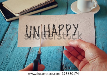 man hand holding card with the text unhappy, cutting the word un so it written happy.  retro style image
