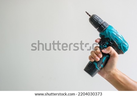 man hand holding cordless screwdriver with wall background, Carpenter working with electric screwdriver on the work
