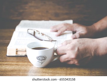 Man Hand Holding A Cup Of Coffee On Wooden Table While Reading Bible In His Devotional Time