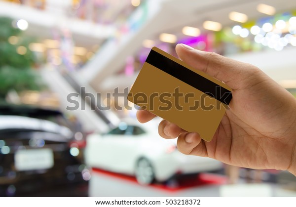 Man\
hand holding empty golden credit or debit card, member card, vip\
card with blurred background of new cars in showroom, or motor show\
event, credit card payment, car insurance\
concept.