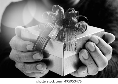 Man Hand Holding A Gift Box In A Gesture Of Giving.blurred Background,black And White