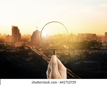 Man Hand Holding A Magnifying Glass, The Cityscape In Focus On Background, Business Vision