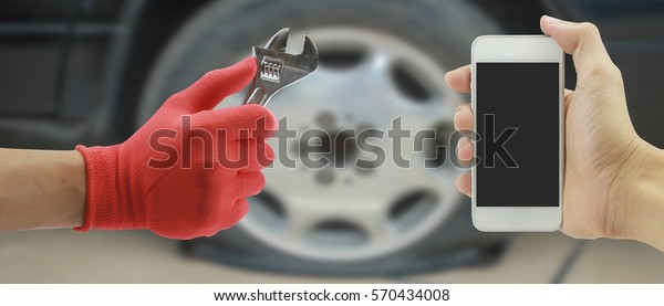 Man hand holding mobile smart phone Contact Car\
repairing,Hand of car technician auto mechanic with a wrench\
working in garage. service in auto repair  Flat rear tire .vintage\
tone,for banner