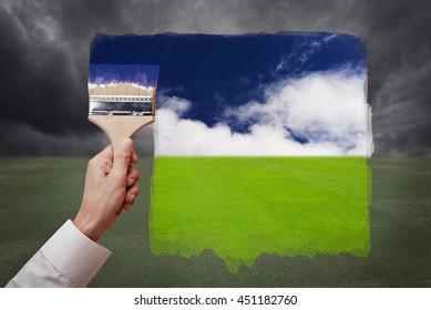 Man hand holding painting brush, paint bright day with blue sky and white cloud on green grass field replace bad cloudy day. Conceptual illustration of new better world or optimistic vision. - Shutterstock ID 451182760