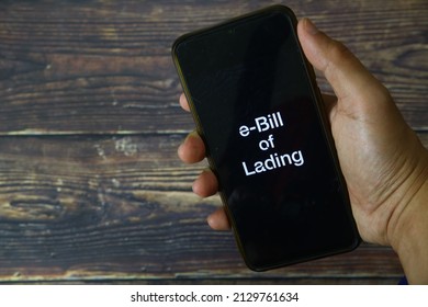 A Man hand holding phone with electronic bill of lading words, an electronic version of the paper bill of lading. Wood background.