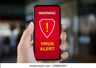 man hand holding phone with warning virus alert alarm on screen background of city street