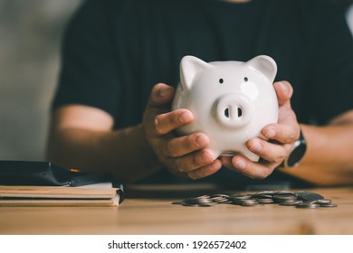 Man hand holding piggy bank on wood table, saving money wealth and financial concept, Business, finance, investment, Financial planning.