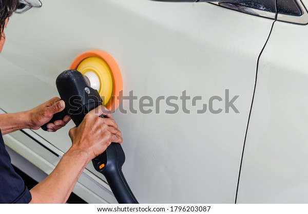 Man hand holding a polishing machine polishing the\
car hood and white.