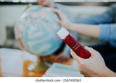 A man hand holding the red bible while lay hand and praying on blurred world globe. christian prayer concept, pray for the world crisis, world mission ministries