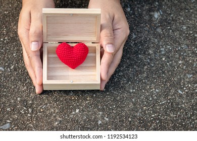 Man Hand Holding A Red Heart In The Wooden Box In The Public Park, For Give Supporting When People Get Who Lack Of Desire With Love Concept.