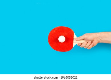 Man Hand Holding A Red Ping Pong Paddle With A White Ball On A Blue Background