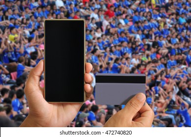 Man Hand Holding Smart Phone And Credit Card On Soccer Fans In A Match And Spectators At Football Stadium