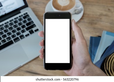 A Man Hand Holding Smart Phone With Laptop And Ear Pod On Wood Desk In Coffee Shop. Mobile With Blank Screen And Can Be Add Your Texts Or Others.