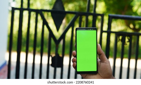 Man Hand Holding The Smartphone With Green Screen Isolated On The Main Entrance Background.