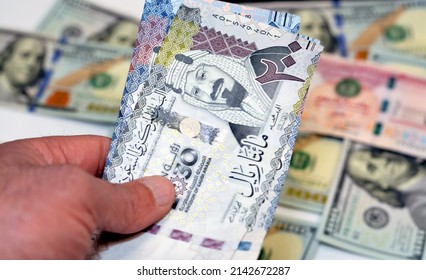 man hand holding a stack of 200 two hundred Saudi riyals banknotes money, spending, giving and using money concept, paying and buying using banknotes on blurred 100 American dollars background