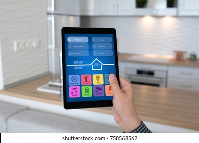 man hand holding tablet PC with app smart home on background room kitchen