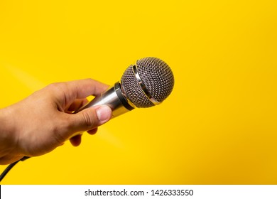 Man Hand Holds Black And Silver Microphone Over Yellow Background