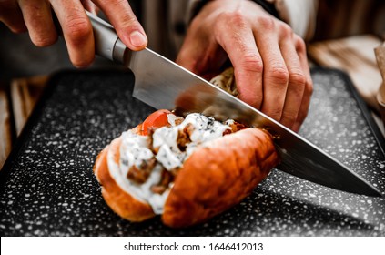 man hand with knife cut Philly cheese steak sandwich with meat, vegetables, cheese and sause on cutting board