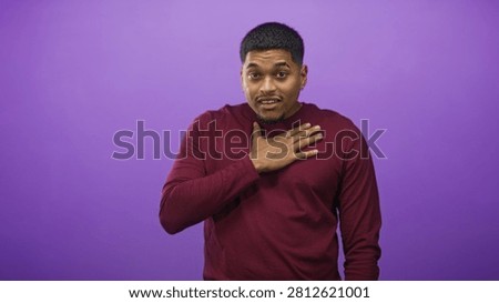 Man with hand on chest and slight shrug in studio purple backdrop, wearing burgundy long sleeve shirt and small earring; apologetic.